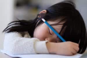 Child with autism spectrum disorder sleeping at her desk, with pencil in hand. 