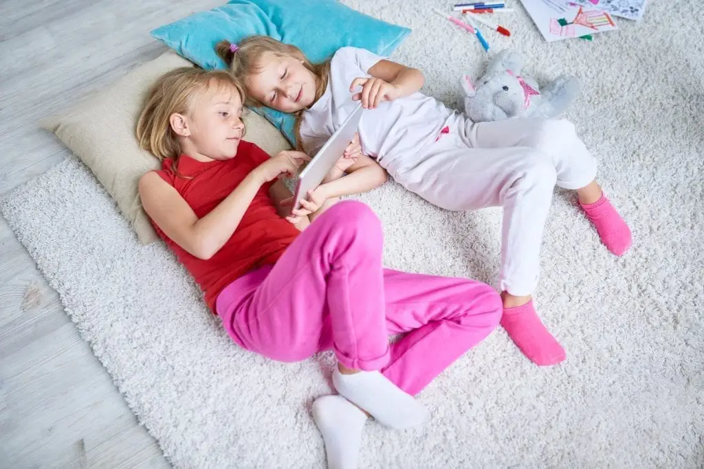 Two young girls laying on the carpet looking at an iPad together during a social skills training in Toronto session. 