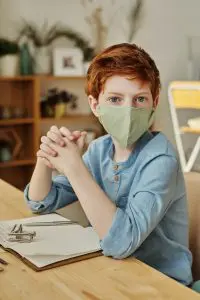 Boy sitting at desk wearing a mask after using applied behaviour analysis to learn to tolerate the mask. 