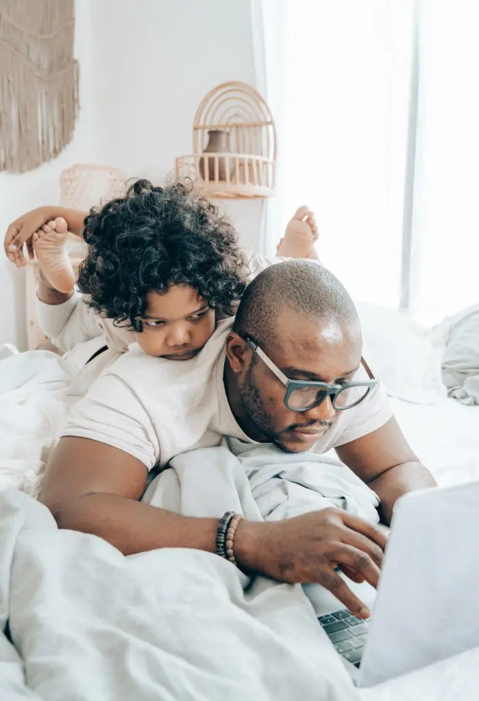 Black father and son laying on a bed reading about how to choose an ABA provider. 