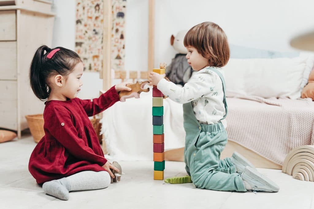 Two kids playing on the floor with blocks. 